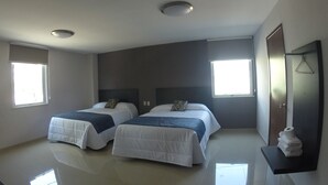 Una habitación de hotel con dos camas, un ventanal grande, un espejo y un perchero.