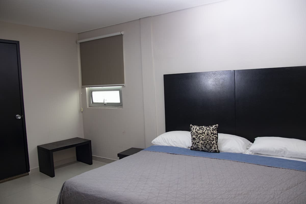 Ein Schlafzimmer mit Bett, Nachttisch, Bank, Fenster mit Jalousien und einer Tür.