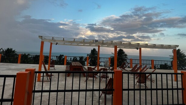 An outdoor seating area with tables and chairs, a pergola, and a view of the sea. - Enjoy Hotel (Caye Caulker)