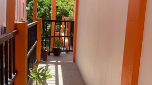 A corridor with tiled flooring, orange walls, and black railings. There are potted plants along the corridor. - Enjoy Hotel (Caye Caulker)