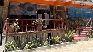 A multi-story building with a 'WELCOME' sign, outdoor plants, and a staircase. - Enjoy Hotel (Caye Caulker)