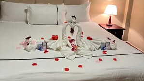 A neatly made bed with a heart-shaped towel arrangement and rose petals. - Enjoy Hotel (Caye Caulker)