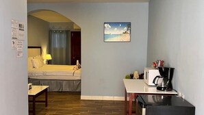 A compact hotel room with a bed, a small dining table, a refrigerator, and a painting on the wall. - Enjoy Hotel (Caye Caulker)