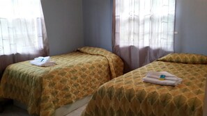A room with two single beds, each with a patterned bedspread and a folded towel on the bed. - Buttercup Cottage Apartments (Arnos Vale)