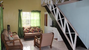 A living room with a sofa, two armchairs, a staircase, and a window with curtains. - Buttercup Cottage Apartments (Arnos Vale)