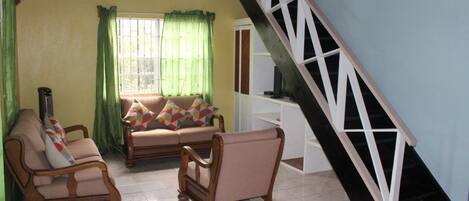 A living room with a sofa, two armchairs, a staircase, and a window with curtains.