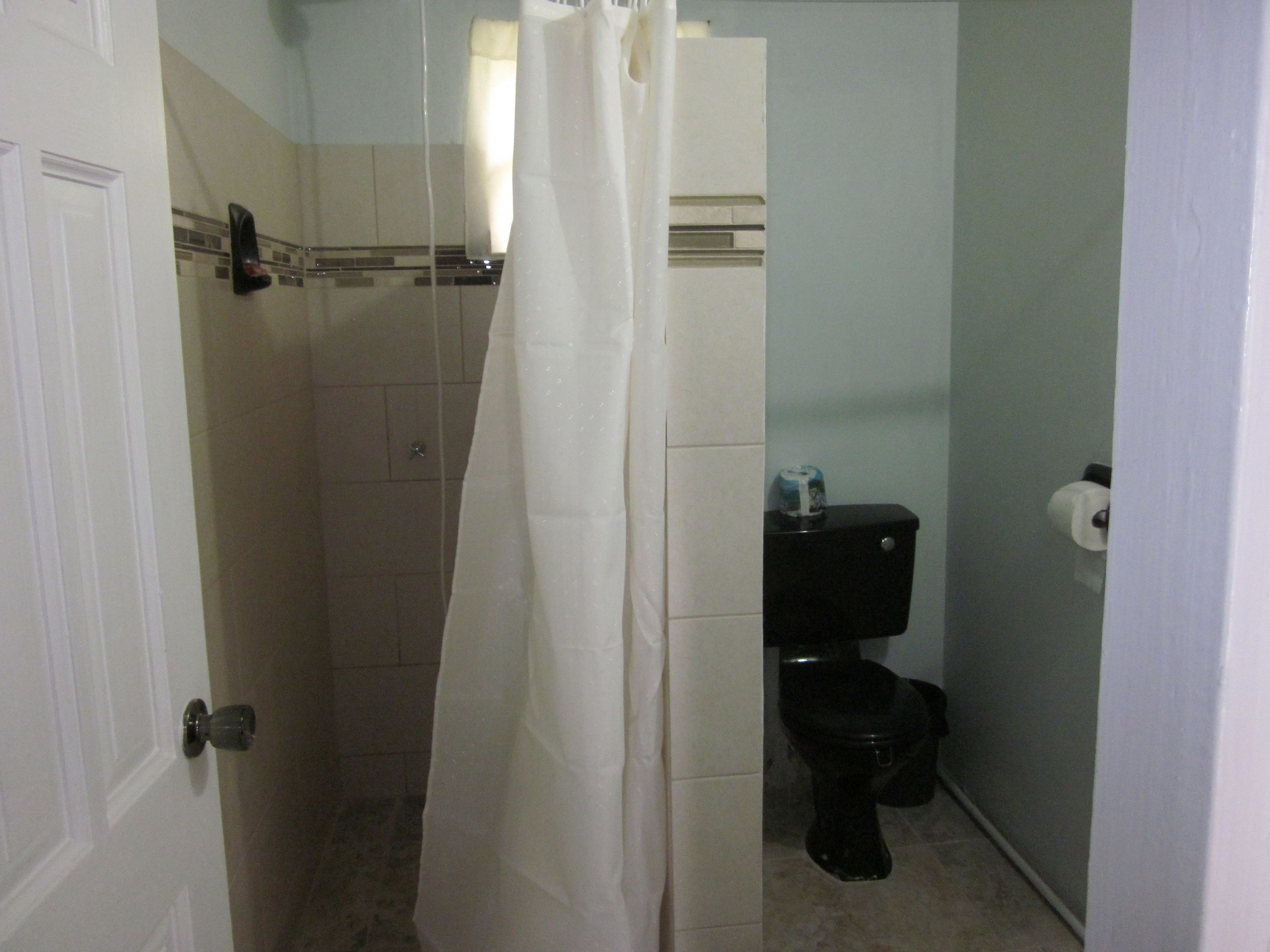 Un baño con cortina de ducha, inodoro y toallero.