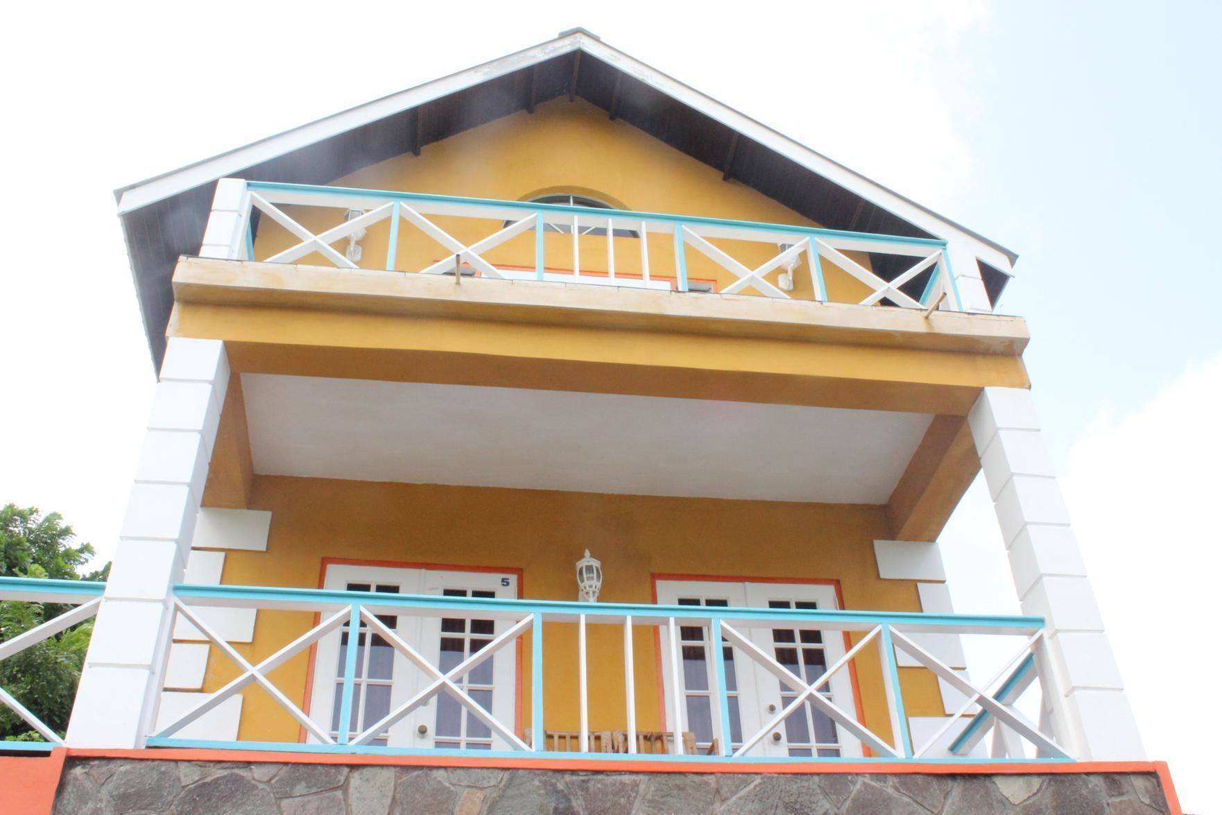 A two-story building with a yellow facade, white railings, and a stone base.