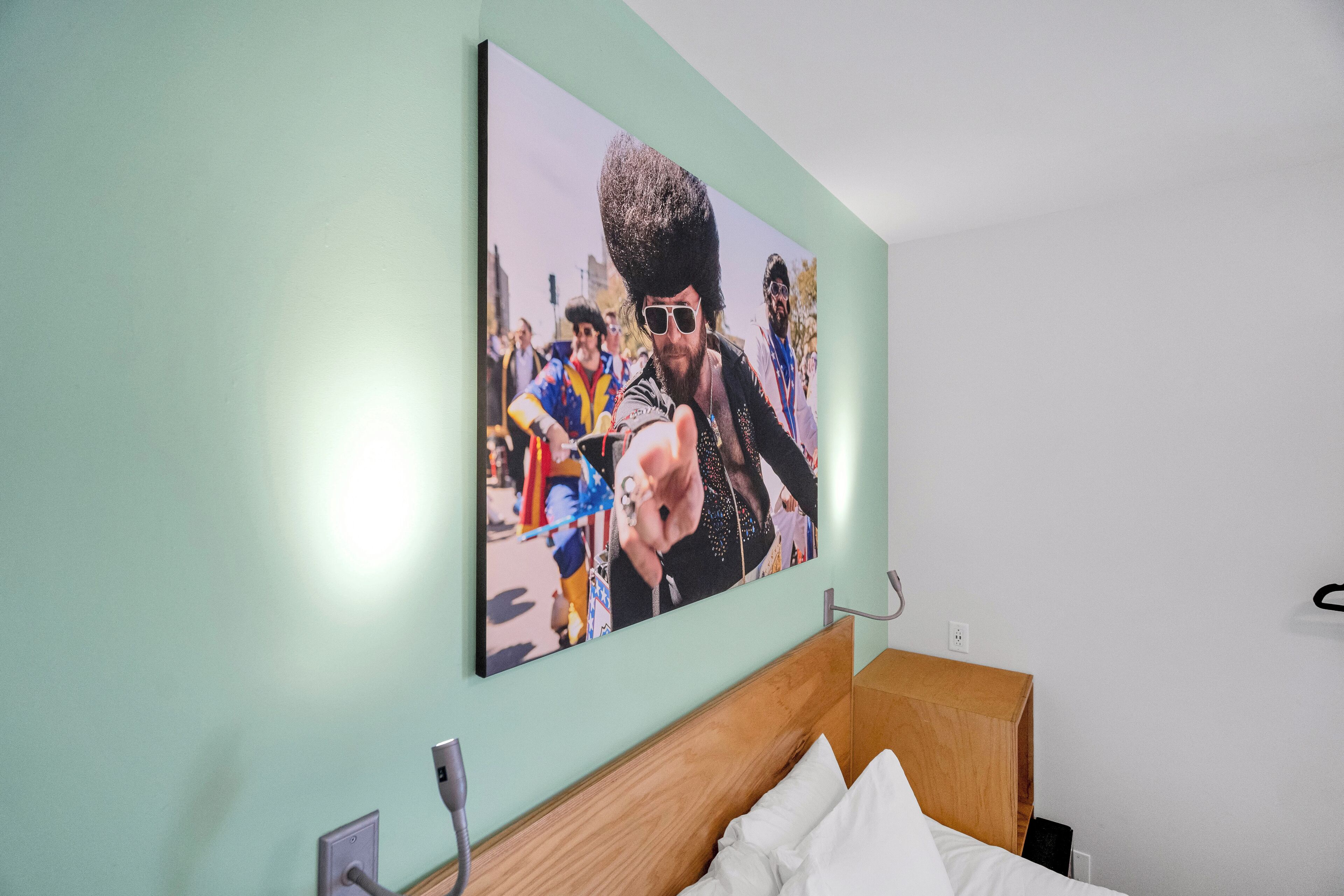 Habitación de hotel con una cama grande, cabecera de madera y una obra de arte en la pared que representa a un grupo de personas con atuendo colorido.