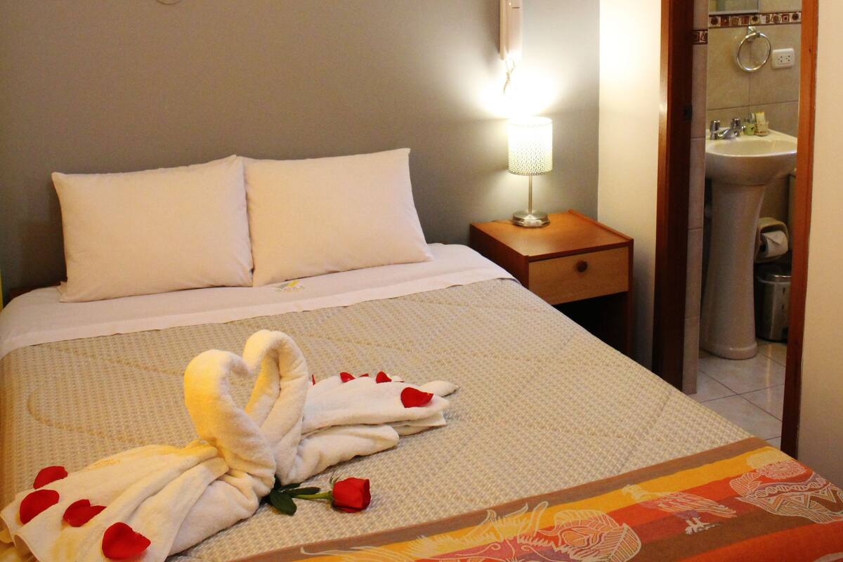 Une chambre d’hôtel avec un lit, une lampe de chevet, un tableau au mur et une salle de bain visible à travers une porte ouverte.