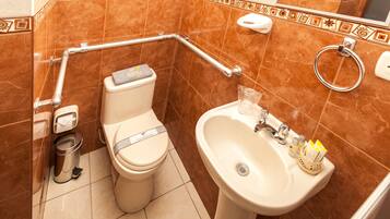 Un baño con inodoro, lavamanos y barras de apoyo.
