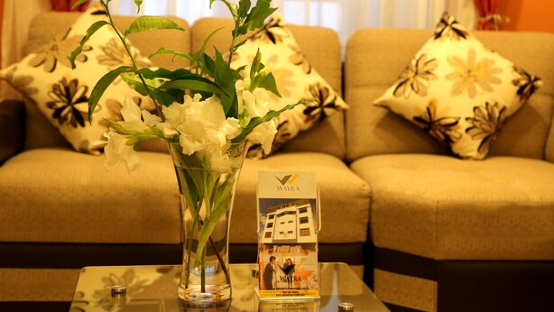 A living room with a sofa, floral cushions, a glass vase with white flowers, and a Wayra hotel brochure on a glass table.