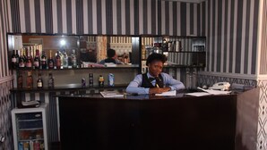 Angolo bar con un bancone, un frigorifero pieno di bevande e scaffali con bottiglie e bicchieri.