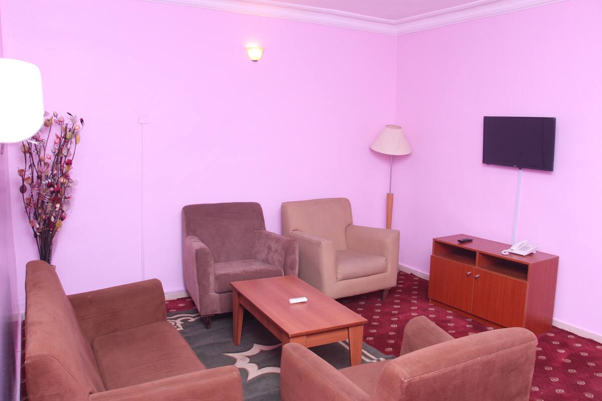 A room with a pink wall, a wooden cabinet, a television, and two chairs.
