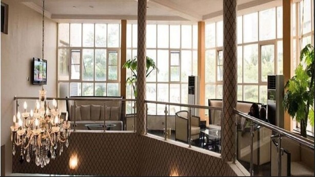 Un'ampia hall d'albergo con soffitto alto, ampie finestre, un lampadario e una scalinata.