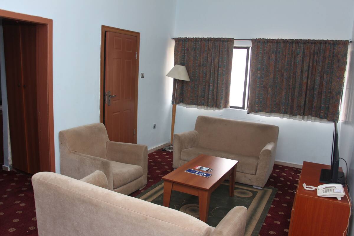 A living room with two beige armchairs, a wooden coffee table, a lamp, and a telephone on a desk.