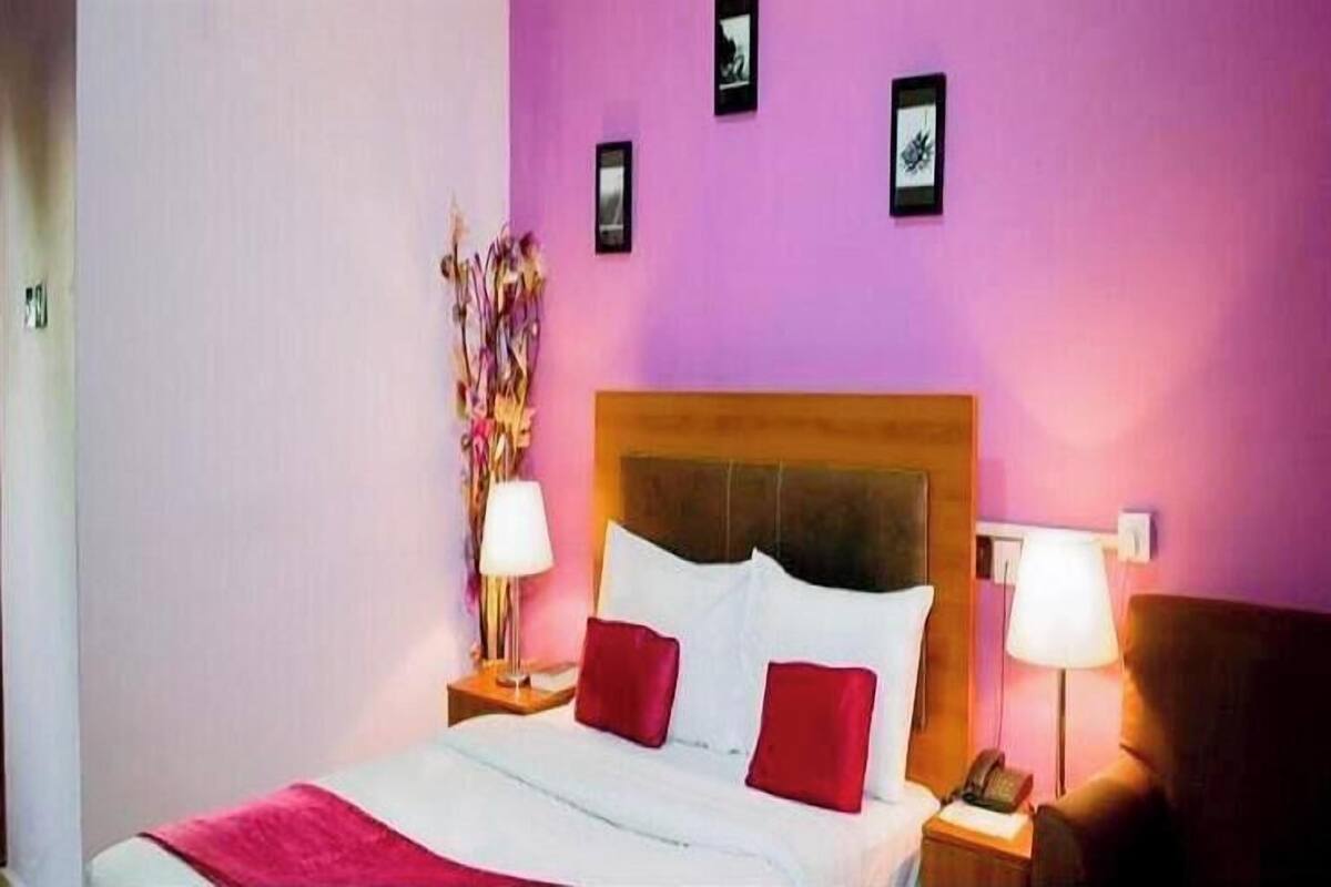 A hotel room with a bed, two bedside tables, a lamp, and a wall with framed pictures.