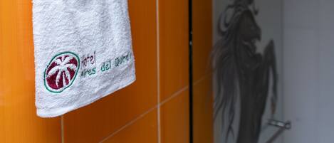 Une salle de bain avec des carreaux orange, une serviette blanche suspendue à un anneau en métal et une porte de douche en verre.