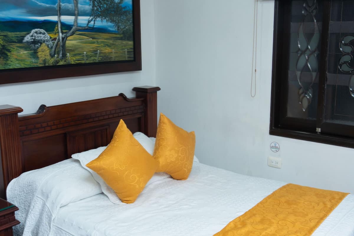 Ein ordentlich eingerichtetes Schlafzimmer mit einem hölzernen Bett, weißer Bettwäsche und einer gelben Tagesdecke.
