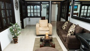 A living room with a beige armchair, a brown sofa with patterned cushions, a glass coffee table, and a small potted plant. - Hotel Aires Del Quindio (Armenia)