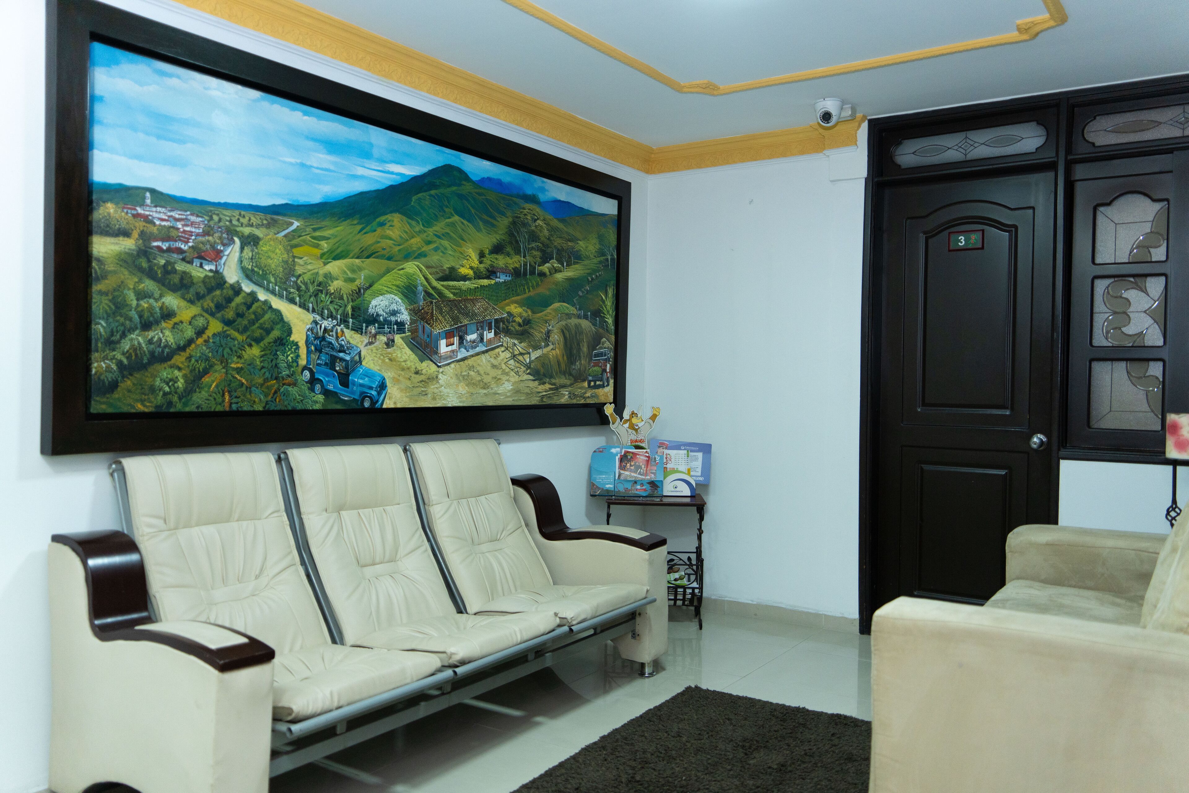 A living room with a large landscape painting, a sofa, a small table with a box, and a door with a number.