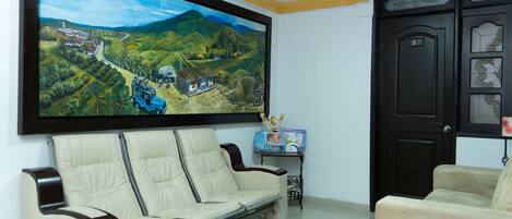 Una sala de estar con un cuadro de paisaje grande, un sofá, una mesita con una caja, y una puerta con un número.