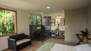 A modern bedroom with a large bed, a sofa, a bathroom with a shower, and a view of greenery. - Finca Cafetera El Balso (Armenia)