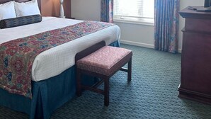 A hotel room with a bed, bedside lamp, bench, dresser, and a window with curtains. - Vacation Village at Williamsburg (Williamsburg)