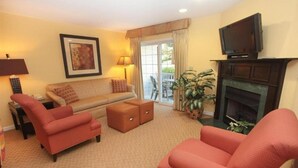 A living room with a sofa, two armchairs, a fireplace, a television, and a large window with curtains. - Vacation Village at Williamsburg (Williamsburg)