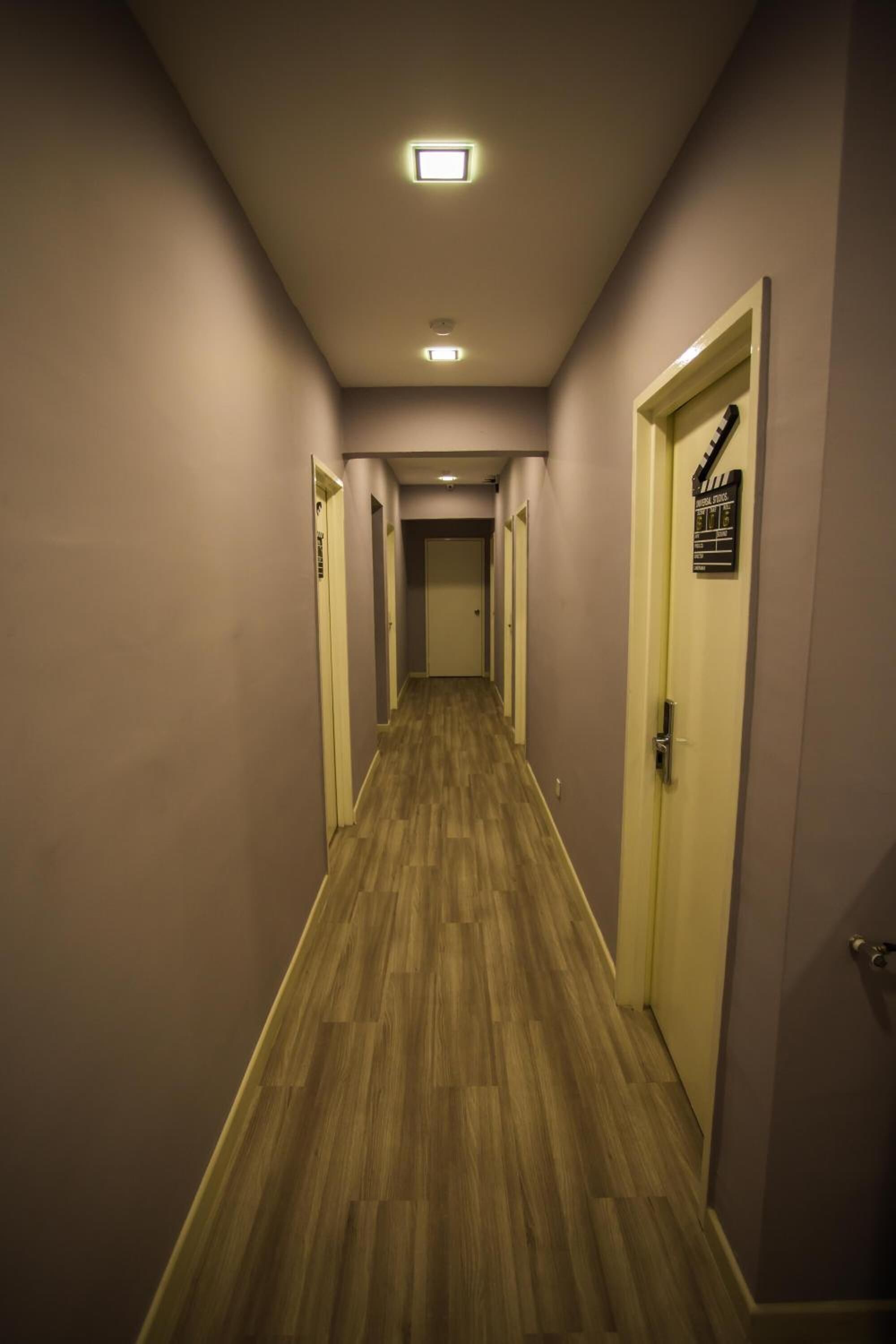 Un couloir doté d’un plancher en bois, d’un luminaire au plafond et d’une porte sur laquelle est affiché un panneau.