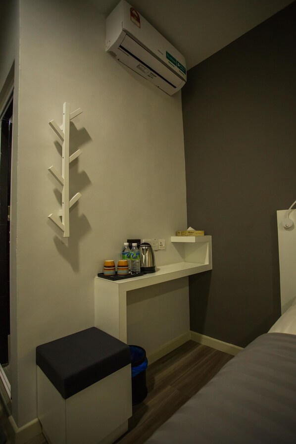 A compact hotel room with a white desk, a small seating area, a bed, and a wall-mounted air conditioner. - Hollywood Hotel (Ipoh)