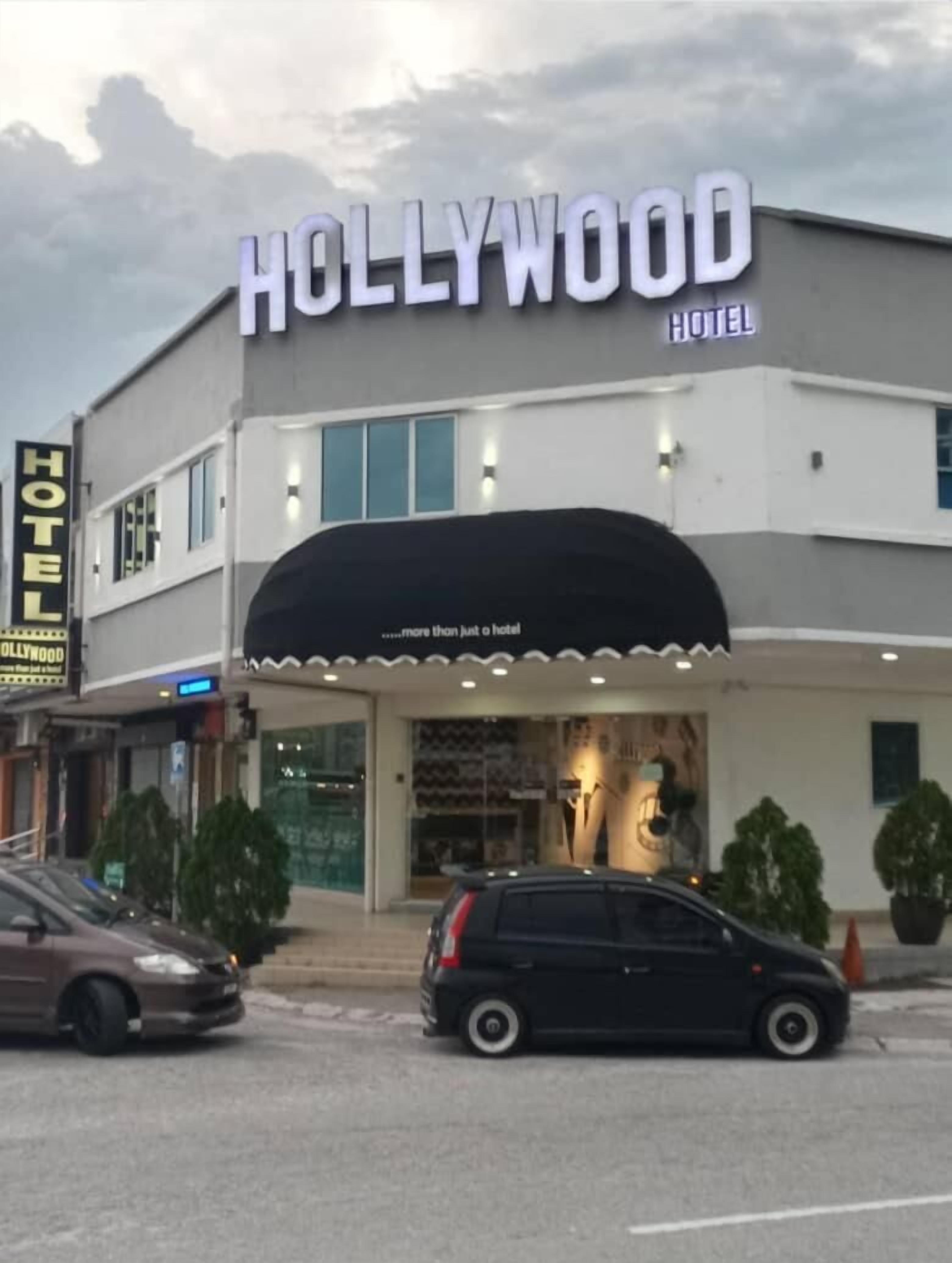 Hotel llamado "Hollywood" con un cartel luminoso, una entrada cubierta y un estacionamiento con coches.