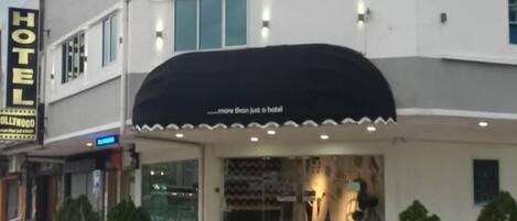 Hotel llamado "Hollywood" con un cartel luminoso, una entrada cubierta y un estacionamiento con coches.