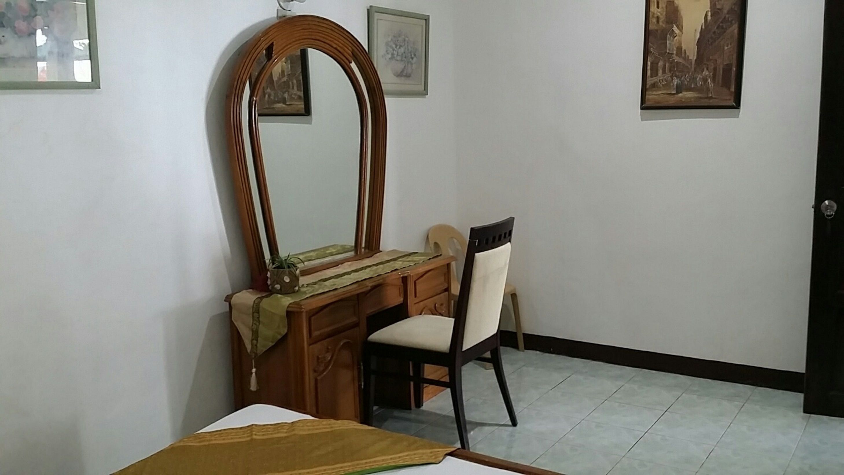 A room with a wooden dresser, a mirror, a chair, and a bed. There are framed pictures on the wall.