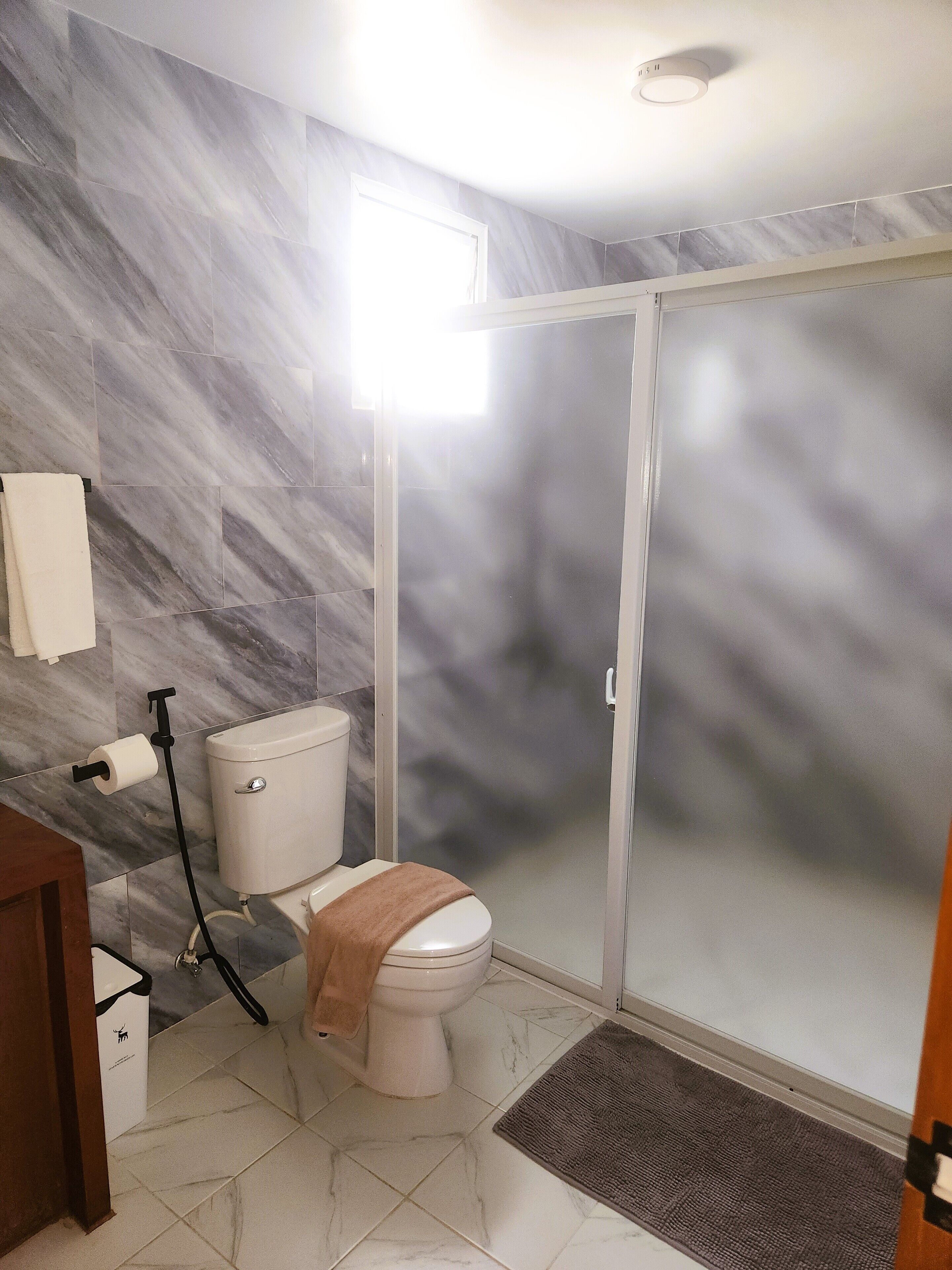 A bathroom with a toilet, a shower enclosure, and a marble-tiled floor.