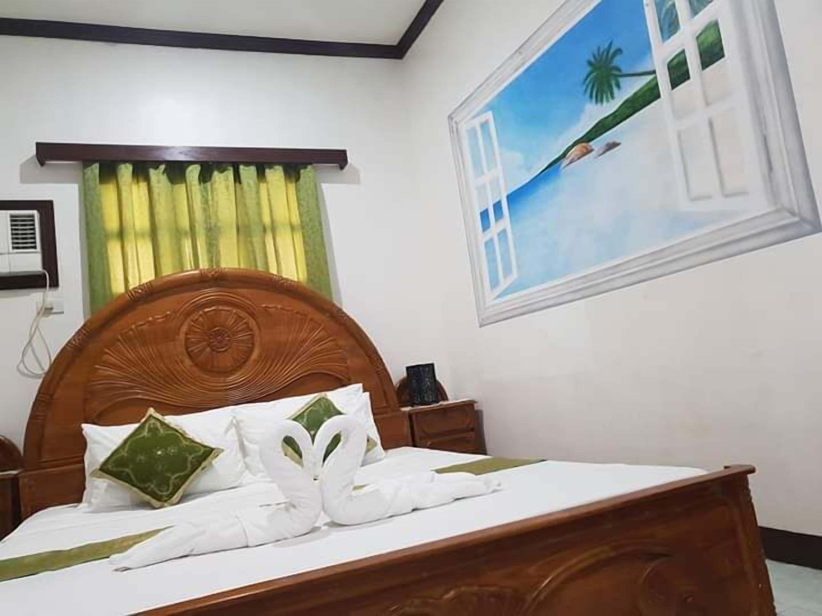 A neatly made bed with a wooden headboard, a painting of a beach scene on the wall, and a window with curtains.