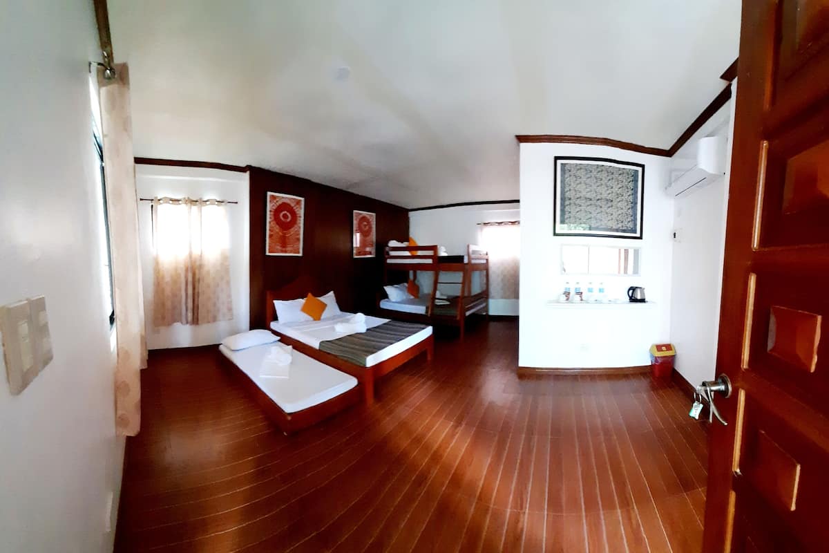 Quarto com cama, uma mesinha, uma cadeira e um pequeno espaço com cozinha.