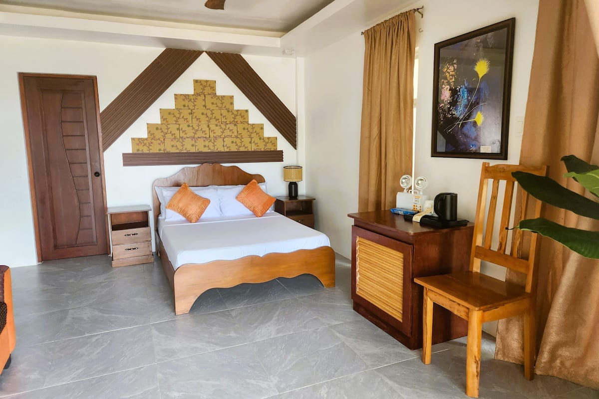 Quarto de hotel com uma cama, uma escrivaninha, uma cadeira, uma porta e uma parede com um painel decorativo.