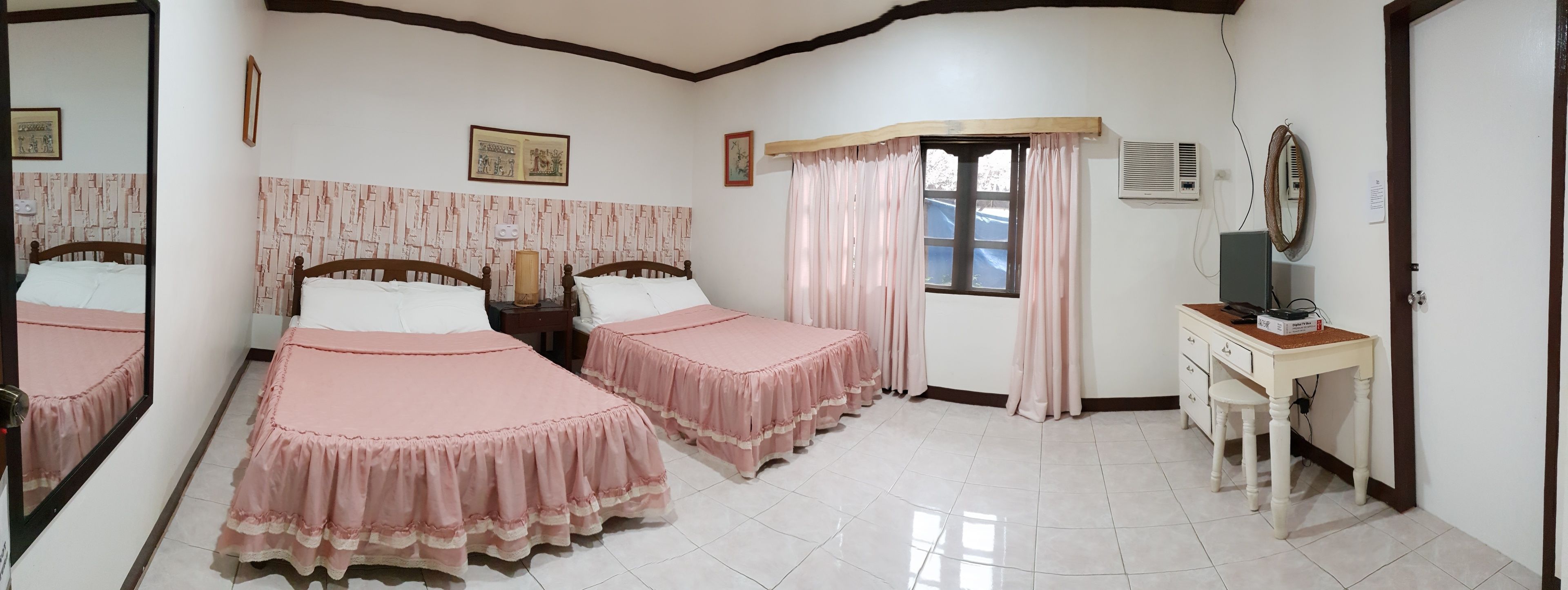 A room with two beds, a desk, a mirror, and a window with curtains.