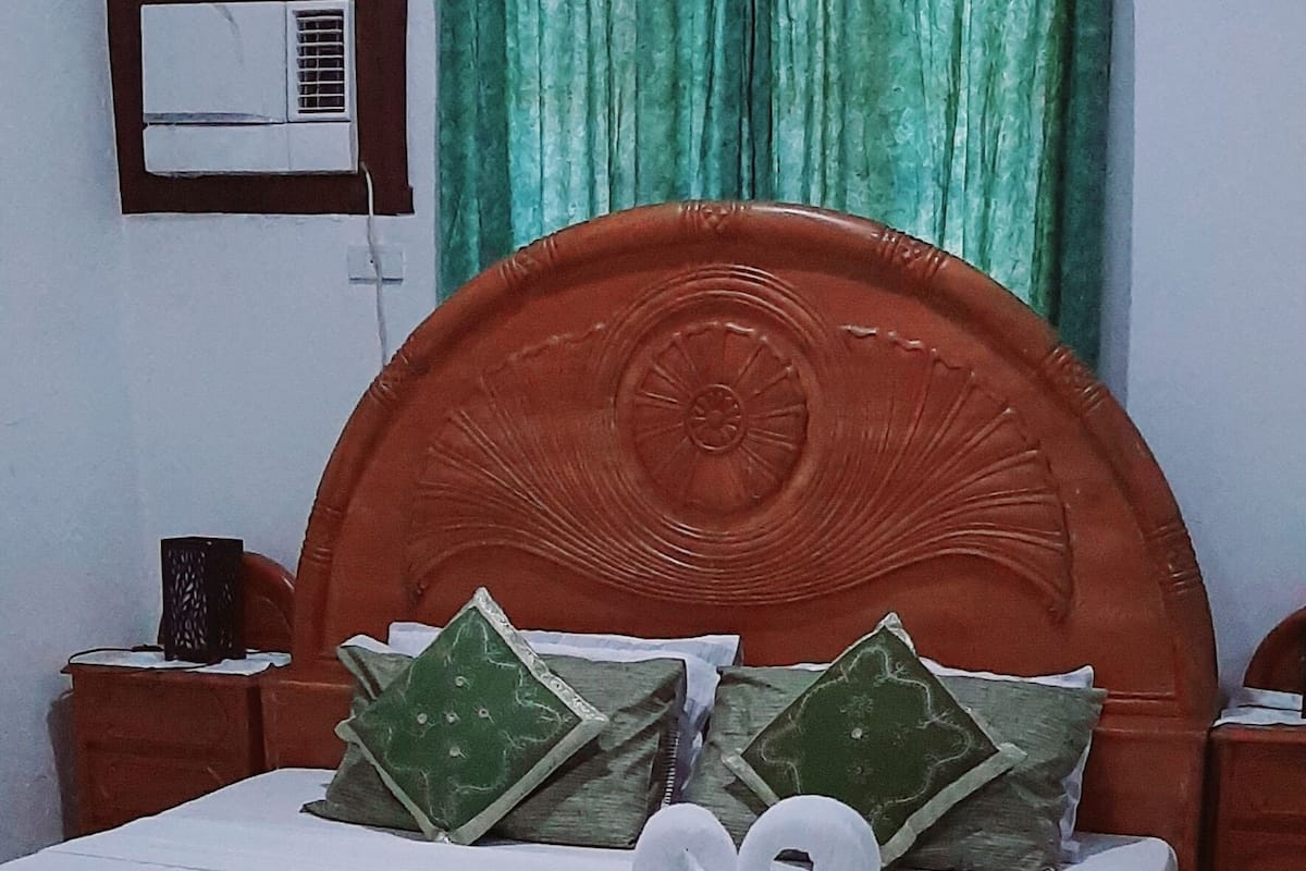 Uma cama bem arrumada com lençóis brancos e almofadas verdes, uma cabeceira de madeira e uma cortina verde.