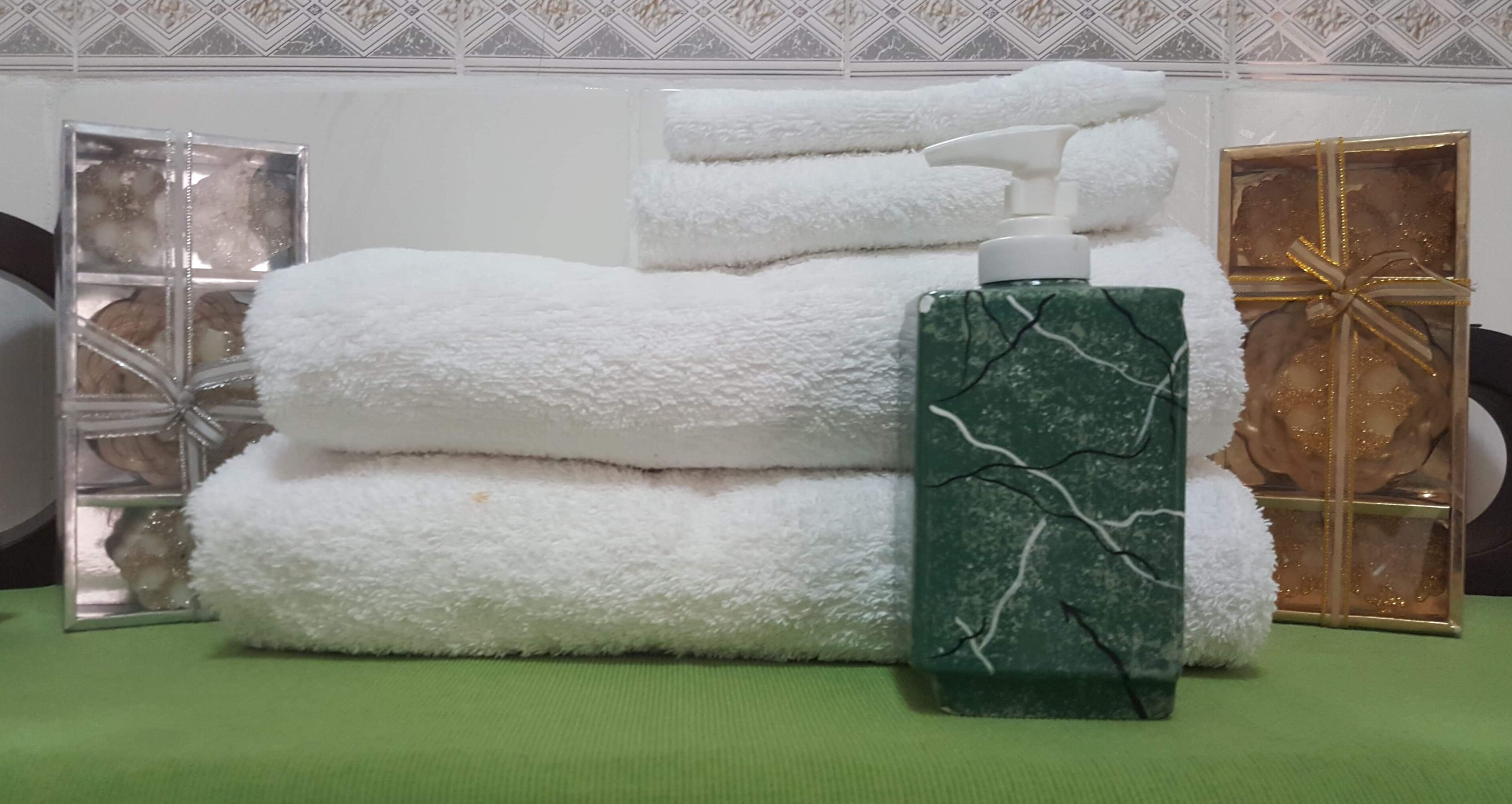 A stack of white towels, a green marble bottle, and a gift box on a green surface.