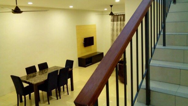 Un comedor con una mesa y sillas, un televisor montado en la pared, y una escalera con barandilla de madera.