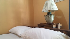 A neatly made bed with white linens and a single white pillow, a wooden nightstand with a lamp, and a wall socket. - Zleep63 - Hostel (Bangkok)