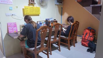 A dining area with wooden chairs and tables, a red backpack on the floor, and various signs on the wall.