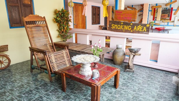 A room with a wooden chair, a table with a vase of flowers, and a sign indicating a smoking area. - Zleep63 - Hostel (Bangkok)