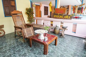 A room with a wooden chair, a table with a vase of flowers, and a sign indicating a smoking area. - Zleep63 - Hostel (Bangkok)