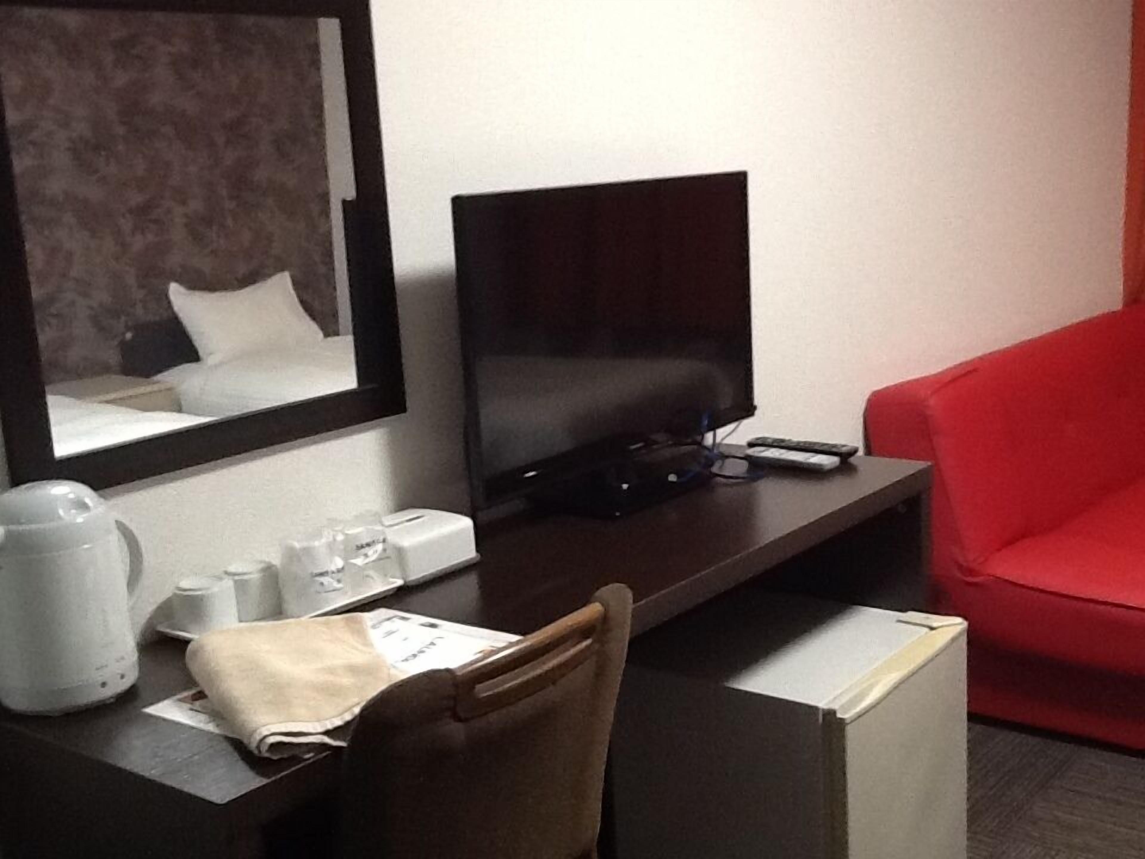 A hotel room with a desk, a flat-screen TV, a red chair, and a mirror.