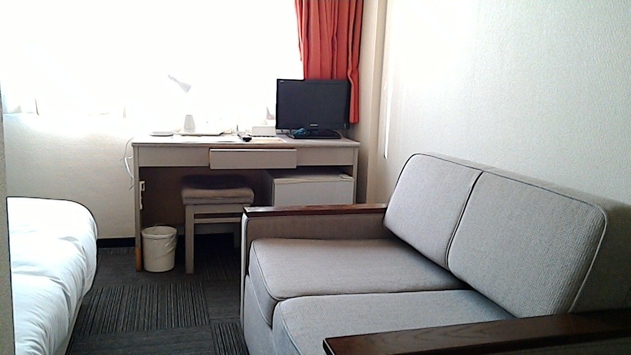 A hotel room with a bed, a desk with a computer, a chair, and a sofa.