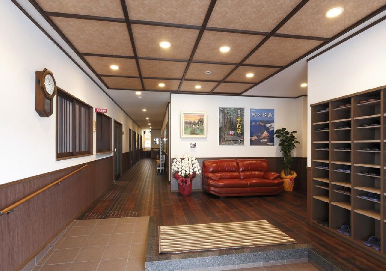 Ein Hotelkorridor mit Holzboden, einem braunen Ledersofa, einem Schuhregal und einer Uhr an der Wand.