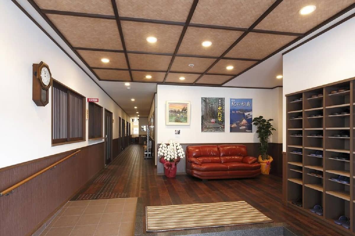 Un couloir d’hôtel avec un plancher en bois, un canapé en cuir marron, un porte-chaussures et une horloge au mur.